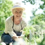 A woman wearing a hat is smiling and planting something new in the garden.