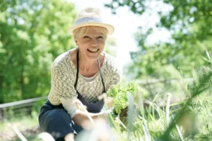 A woman wearing a hat is smiling and planting something new in the garden.