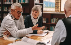 Three adults discuss a play they are reading in a library.