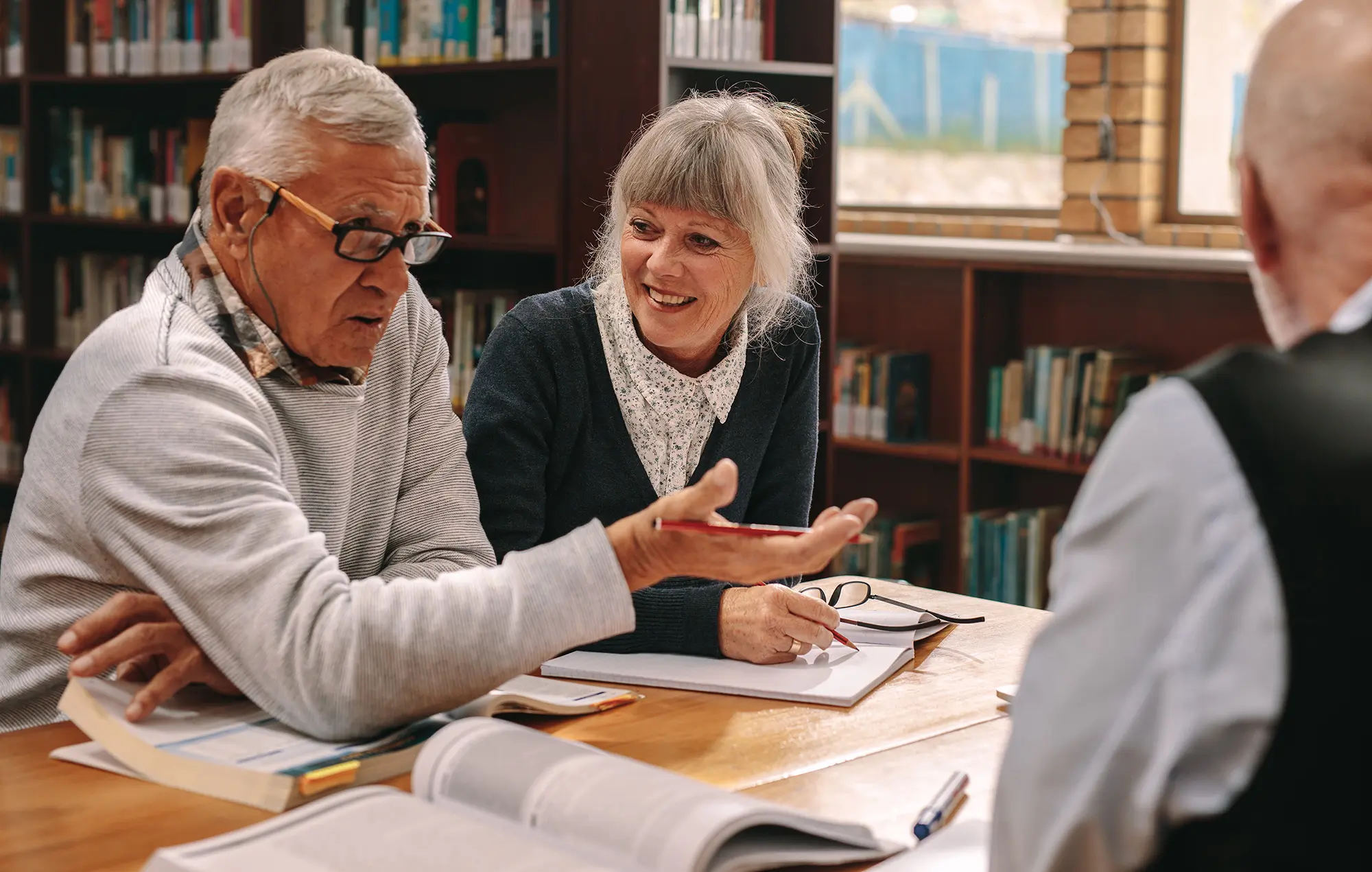 Three adults discuss a play they are reading in a library.