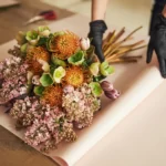 A bunch of flowers have been nicely arranged and are being wrapped in paper.