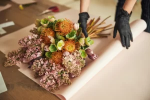A bunch of flowers have been nicely arranged and are being wrapped in paper.