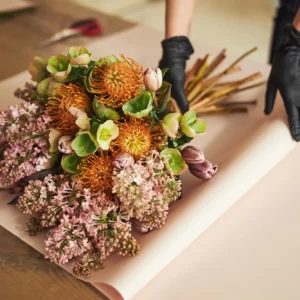 A bunch of flowers have been nicely arranged and are being wrapped in paper.