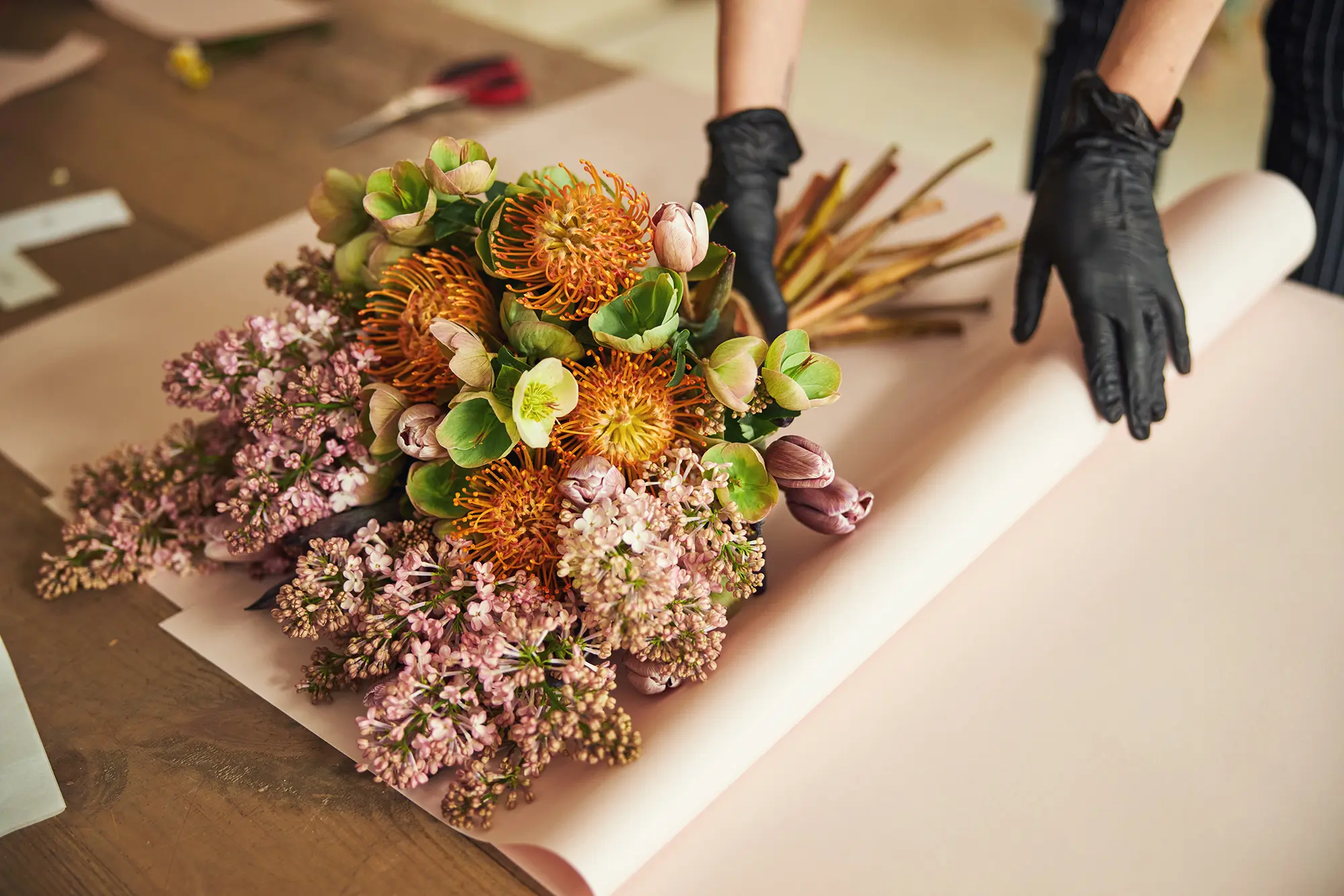 A bunch of flowers have been nicely arranged and are being wrapped in paper.